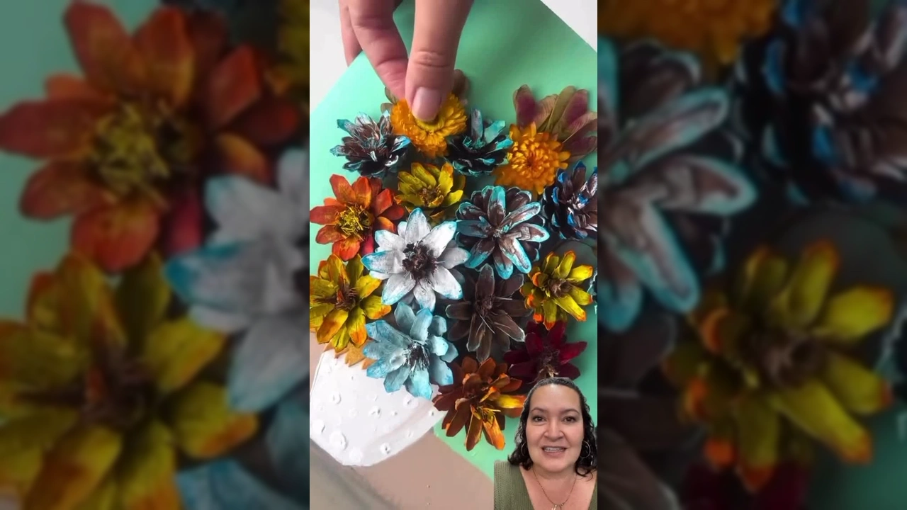 Imagem de uma obra de arte 3D feita com pinhas pintadas em diversas cores, formando um vaso de flores em um painel, com detalhes de folhas e flores desidratadas - Kidica10 | Mel Kiyota