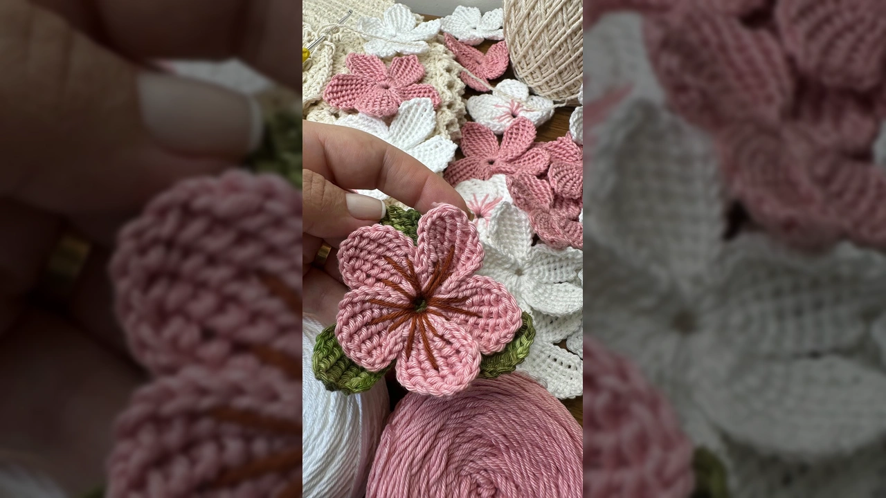 Uma mulher crocheta uma flor de barbante rosa, com muitas flores de crochê rosa e branco espalhadas sobre uma superfície. Créditos: Geise Crochê Criativo / Instagram