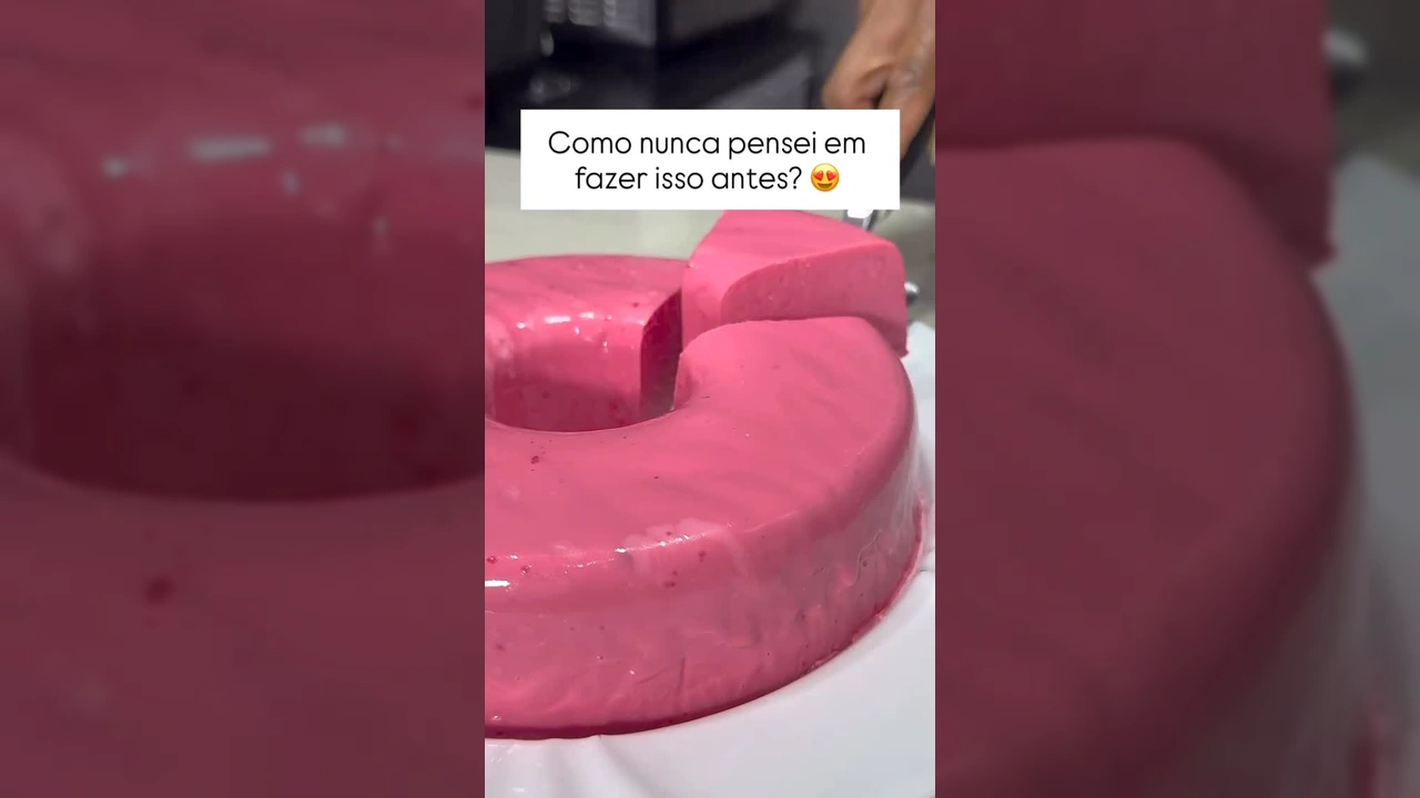 Uma sobremesa rosa vibrante de gelatina e leite condensado cortada em pedaços, com uma calda de chocolate por cima. Créditos para @receiitasdiarias no Instagram.